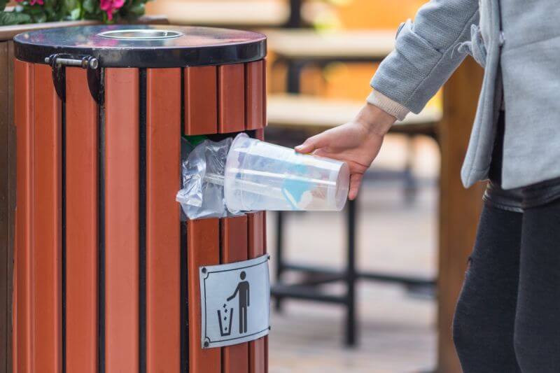 človek vyhadzujúci plastový pohár do vonkajšieho odpadkového koša